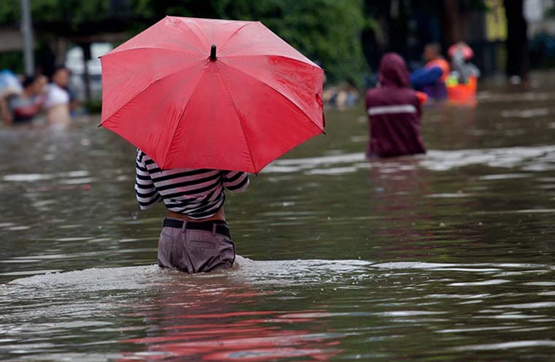 Women walking in waist-deep water, focus of photo is on red umbrella held by woman in striped shirt.