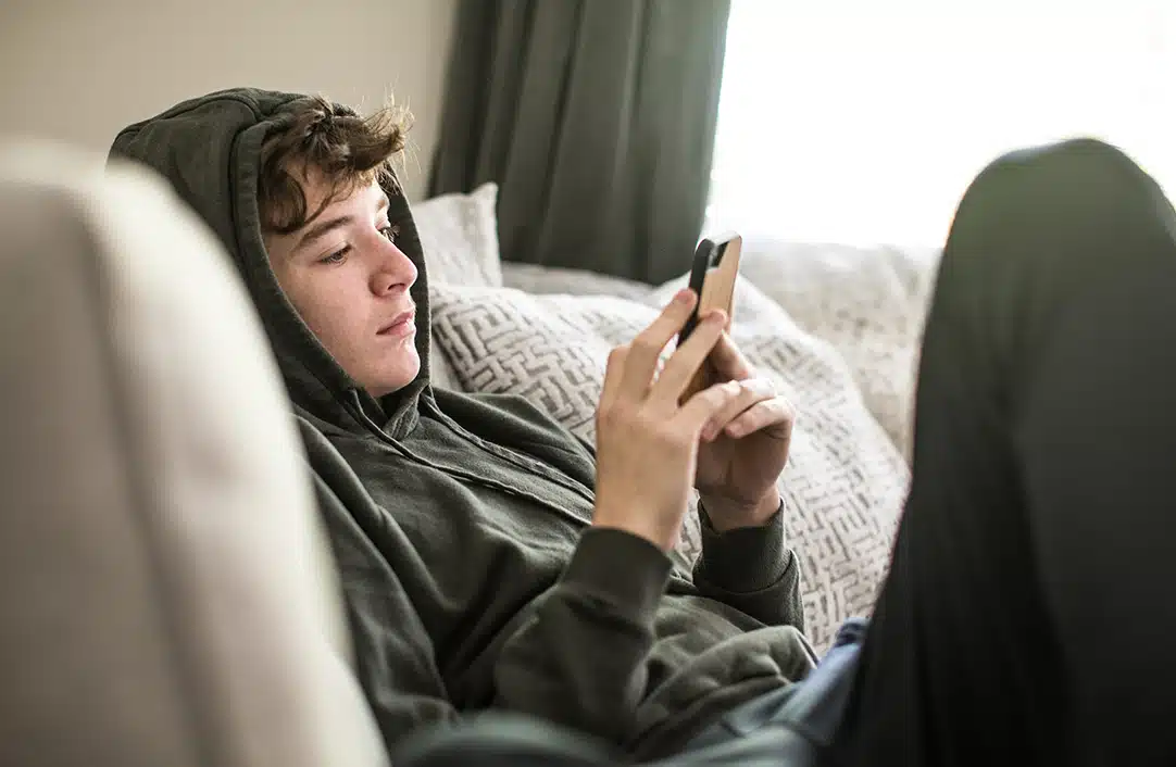 teenage boy looking at phone while sitting on couch