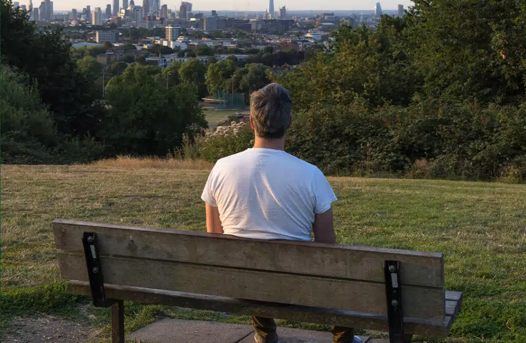 Middle aged man sitting on park bench looking out at city