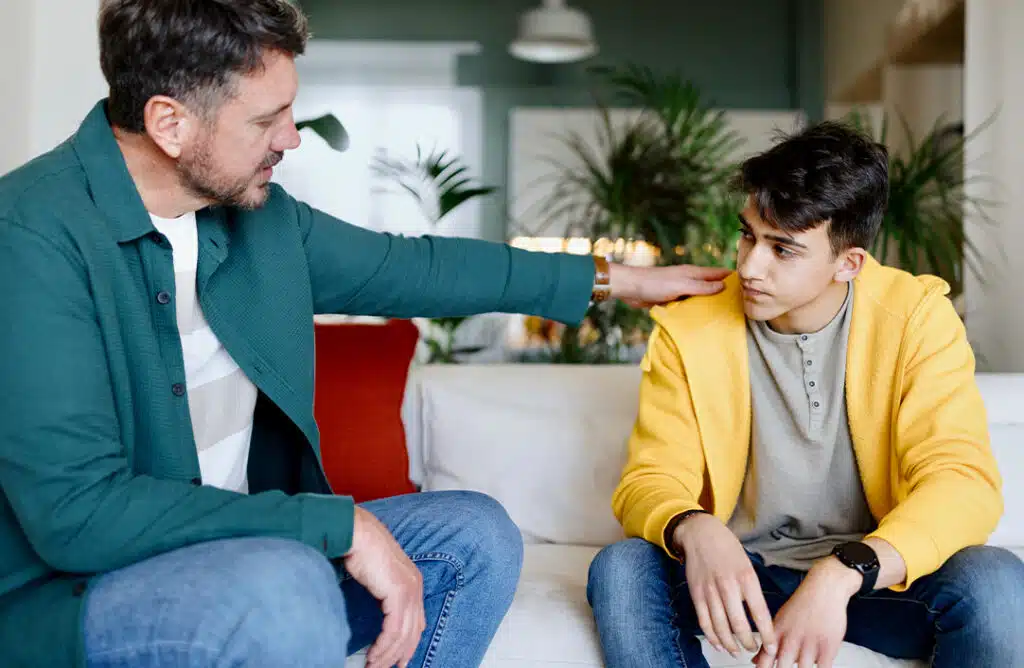Dad with his hand on his son's shoulder sitting on a couch having a conversation