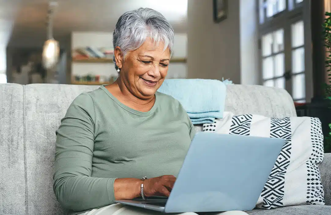 Senior Hispanic Woman working from home on laptop while sitting on sofa.